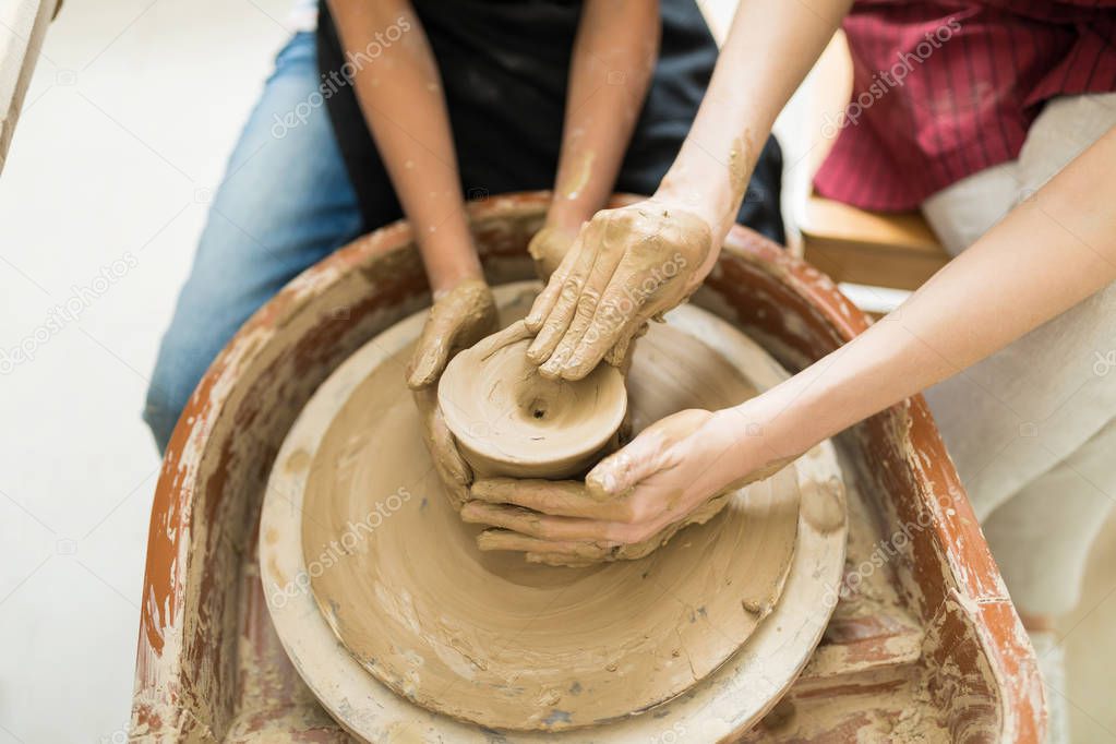 Overhead view of tutor's and girl's hands molding clay on wheel in pottery class