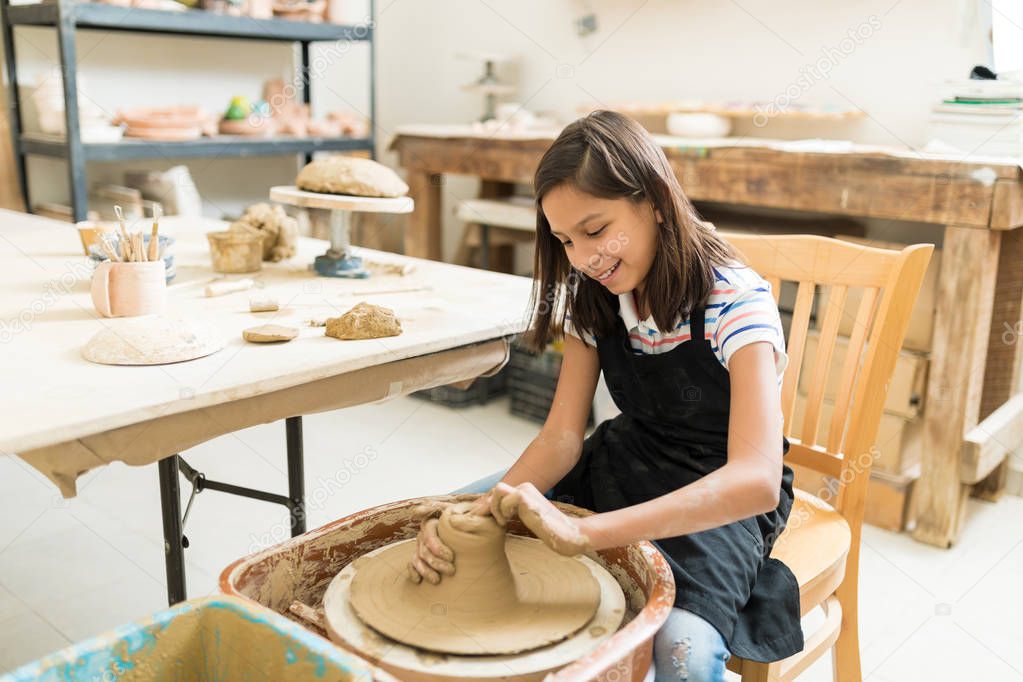 Happy preteen girl pursuing hobby of pottery while sitting in class