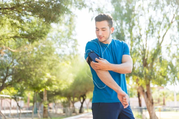 ハンサムな男性ランナー公園でスマート フォンを使用してイヤホンで音楽を聴く — ストック写真