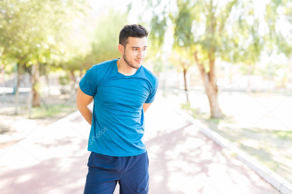 Confident jogger doing stretching exercise while standing on road in park