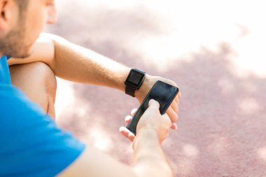 Kırpılmış görüntü fitness Park izlemek için genç adamın smartwatch ve cep telefonu eşitleme