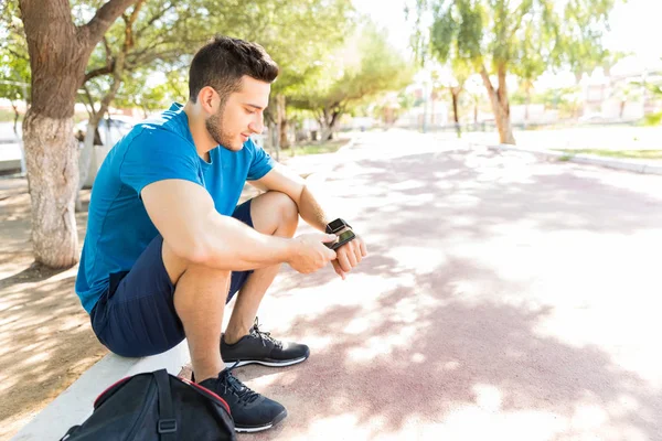 Manliga Löpare Använder Smartwatch Och Telefon När Sitter Parken Solig — Stockfoto