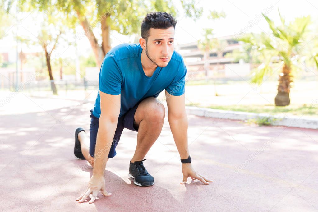 Focused male athlete looking away while taking position at starting line in park