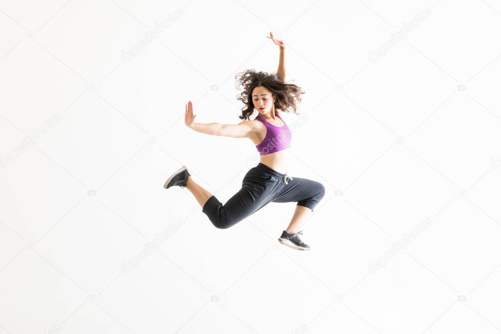 Enthusiastic young woman in midair practicing ballet moves against white background
