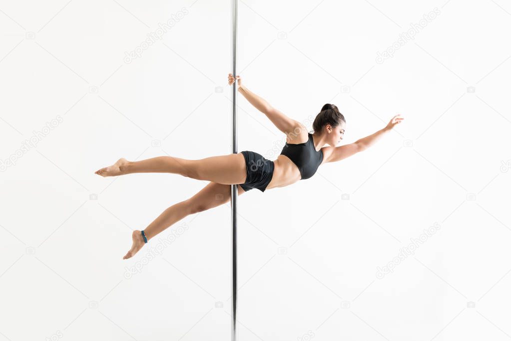 Fit pole dancer with arm raised balancing over white background