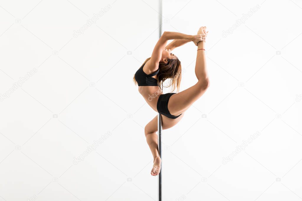 Side view of pole dancer arching body and holding leg while performing in studio