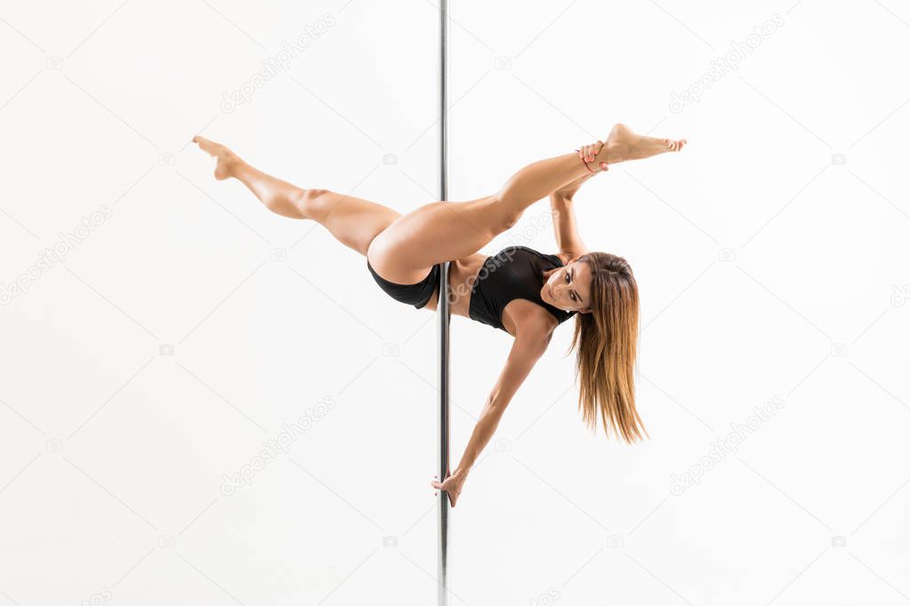 Sexy woman practicing some moves on a pole while dancing on white background