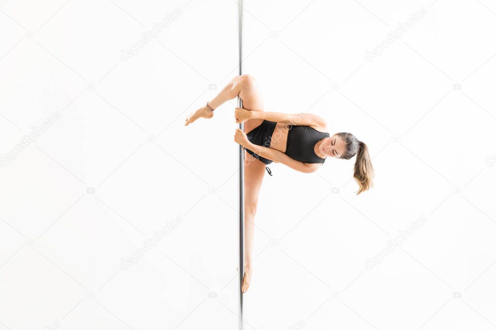 Passionate female practicing amazing positions of pole dance over white background