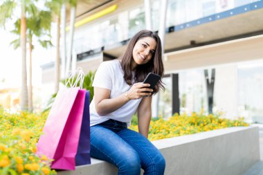 Alışverişkoliğin kadın sosyal ağ üstünde hareket eden telefon alışveriş merkezi dışında gülümseyen