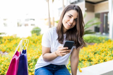 Çanta alışveriş merkezi dışında tarafından otururken smartphone tutan güzel kadın portresi