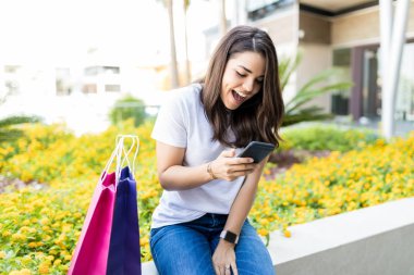 Güzel kadın tarafından alışveriş torbaları mall dışında otururken Smartphone'da SMS okuma şaşırttı