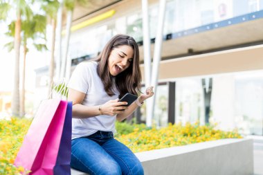 Alışveriş torbaları mall dışında tarafından akıllı telefon kullanan orta yetişkin kadın heyecanlı