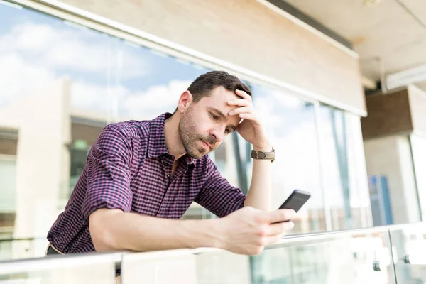 Tensed man reading distressing news on smartphone while leaning on railing in shopping mall