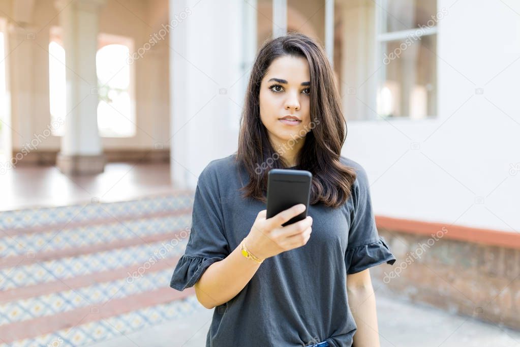 Confident female blogger holding mobile phone while standing outside building