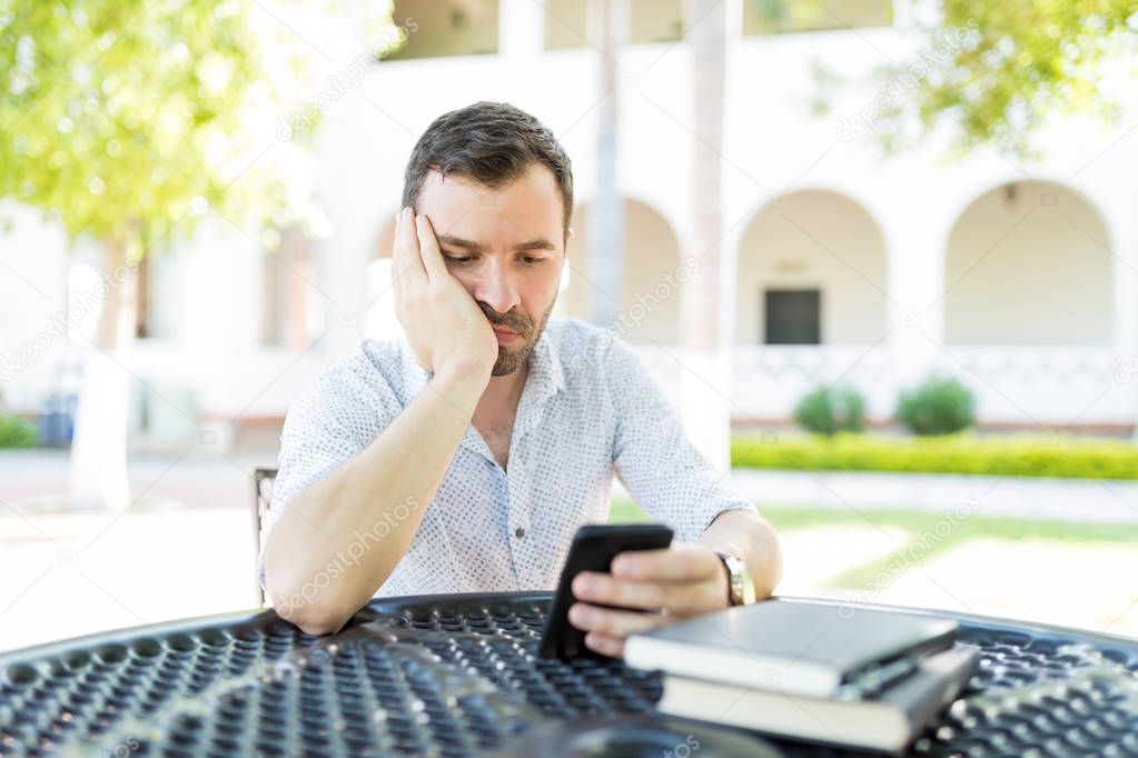 Mid adult man browsing boring websites on smartphone while waiting at table in garden