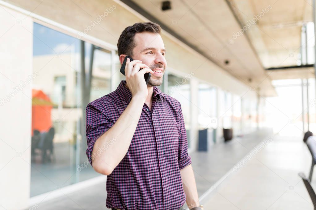 Confident man talking with friend using smartphone in shopping mall