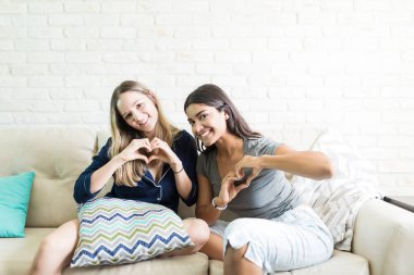 Mutlu genç kadın pijama partisi sırasında kalp şekli el ile yapma