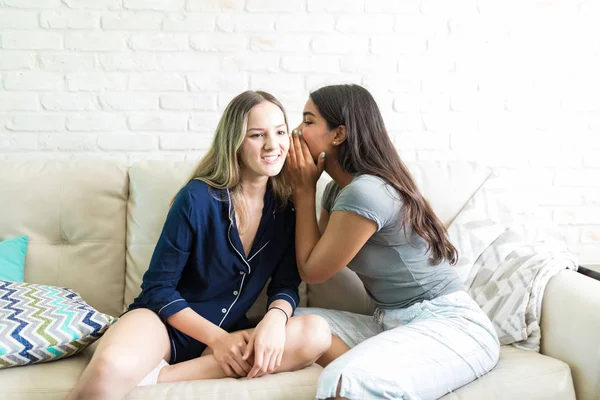 Feminino Sussurrando Segredos Ouvido Melhor Amigo Enquanto Sentado Sofá Casa — Fotografia de Stock