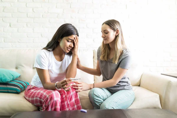 Female Consoling Her Sad Roomie Holding Pregnancy Test Kit Sofa — Stock Photo, Image