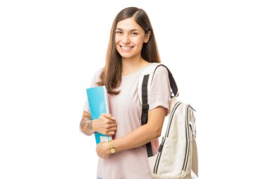 Gülümseyen genç kadın kitap ve beyaz arka plan üzerinde duran sırt çantası ile