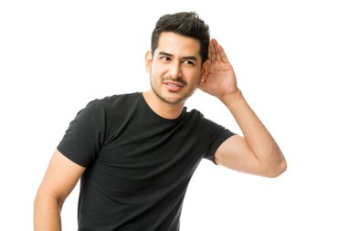 Kulak yakınındaki elini tutarak ve beyaz arka plan üzerinde dikkatle dinleme genç adam