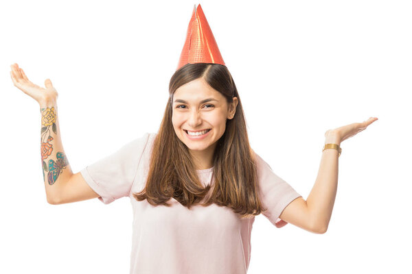 Beautiful young woman wearing paper hat while raising her arms over white background