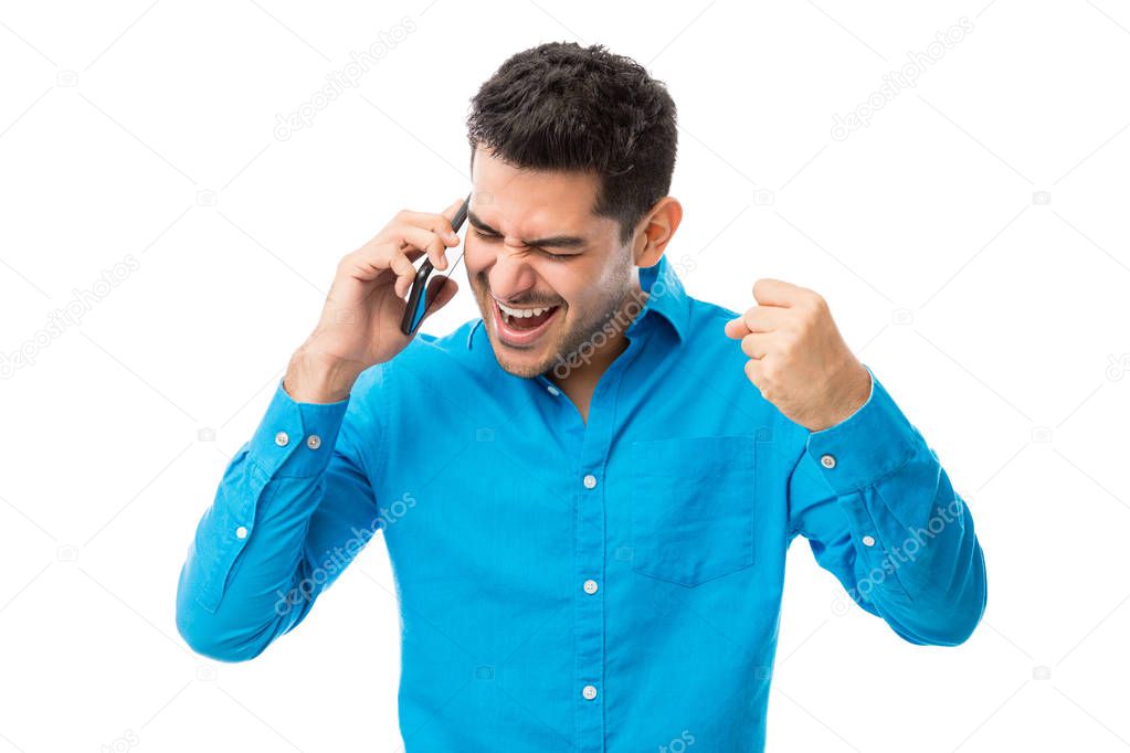 Successful young man receiving good news on mobile phone over white background