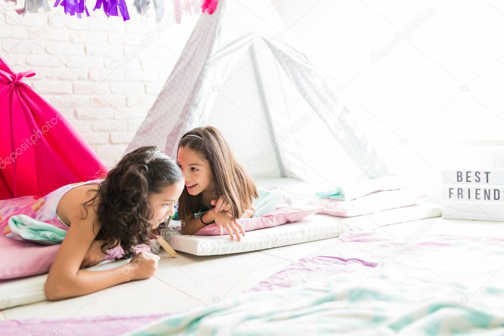 Preteen girl sharing secrets with friend while lying in tipi tent at home