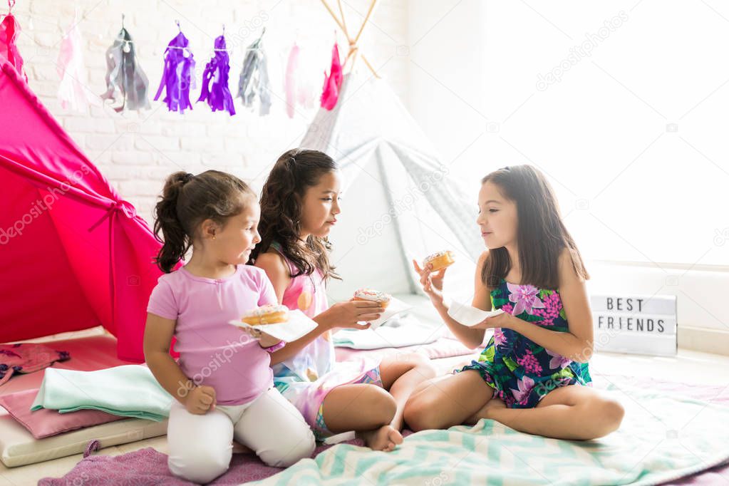 Portrait of cute friends with donuts enjoying sleepover party at home