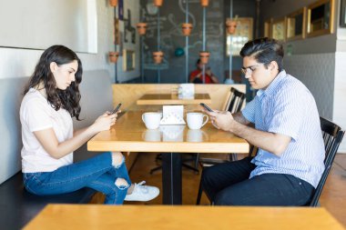 Rude young partners using smartphones while hanging out in coffee shop clipart