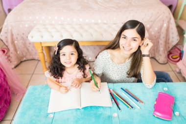 High angle portrait of nanny teaching drawing to cute girl at table clipart
