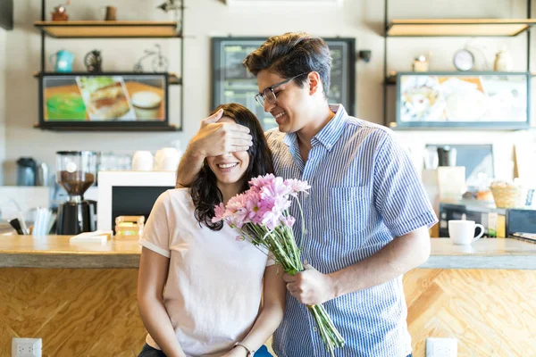 カフェで花束を押しながらのガール フレンドの目を覆っている幸せな若い男 — ストック写真