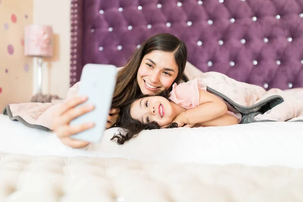 Hispanic Mother Daughter Smiling While Taking Selfie Mobile Phone Bed — Stock Photo, Image