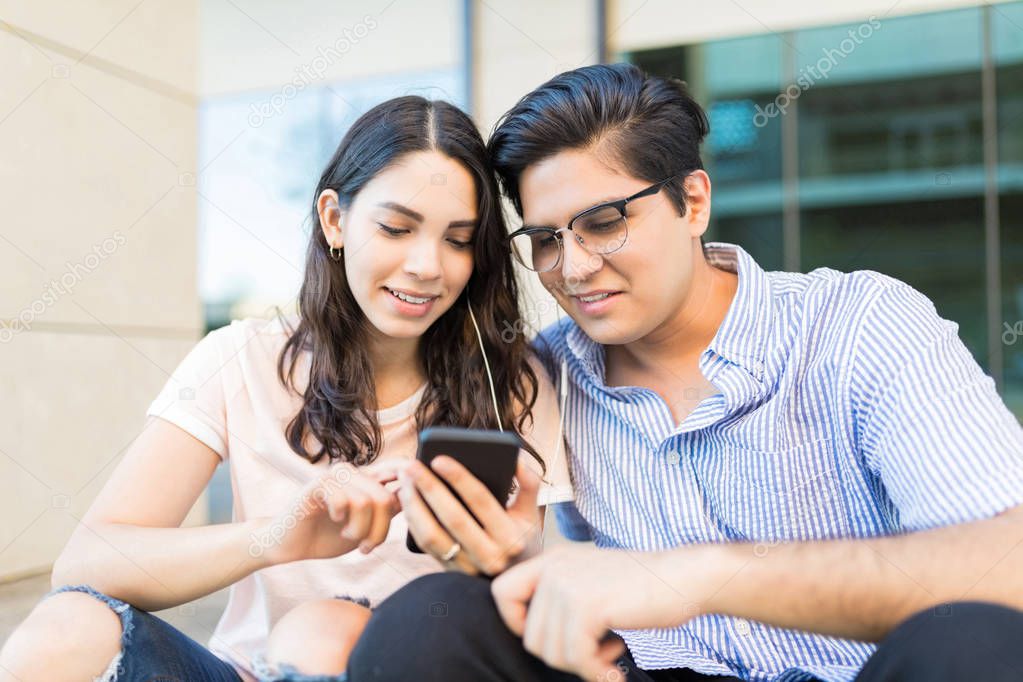 Young Hispanic couple listening to online music on smartphone at shopping mall