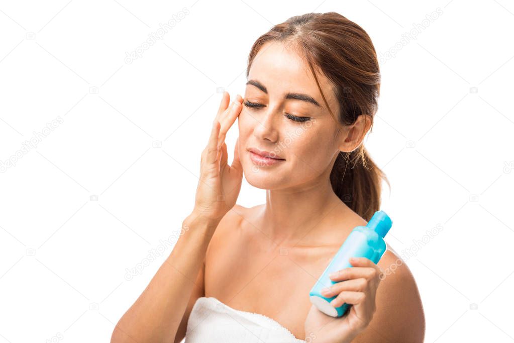 Closeup of glamorous woman applying moisturizer on face over white background
