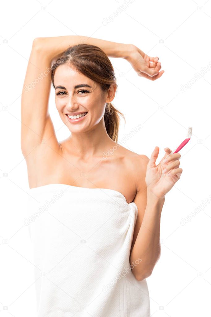 Portrait of smiling mid adult woman wrapped in towel showing her armpit while holding razor against white background