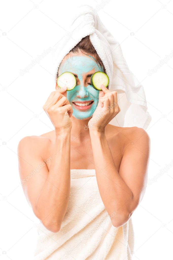 Attractive and smiling Latin woman with hair tied up in towel undergoing beauty treatment against white background