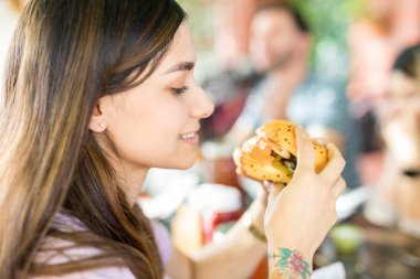 Güzel İspanyol kadın açık restoranda lezzetli sağlıksız hamburger yeme yan görünüm