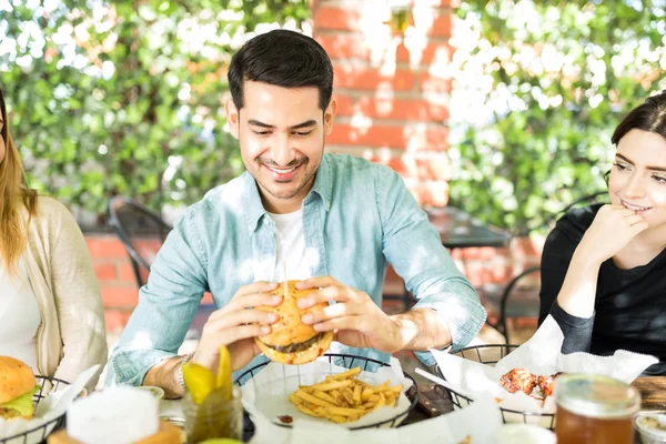 Hombre Encantado Sosteniendo Hamburguesa Deliciosa Durante Reunión Con Amigos — Foto de Stock