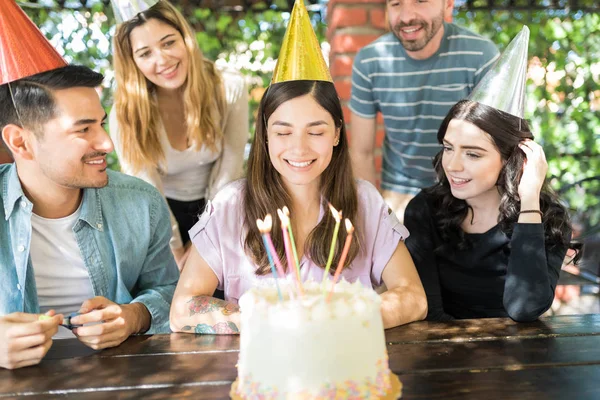 Charming Latin woman in front of cake making birthday wish by friends at table