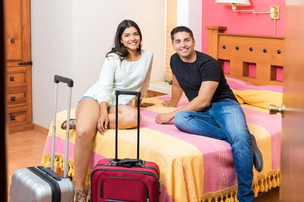 除了酒店房间里的行李外 还有一个微笑的男人和女人坐在床上的肖像 — 图库照片