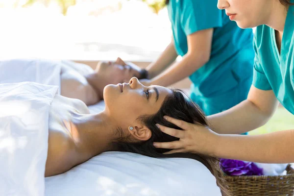 Woman relaxing while lying besides boyfriend during head massage at healthcare spa salon