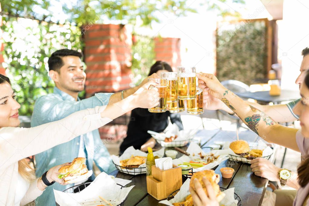 Best buddies toasting beer glasses while enjoying junk food at eatery