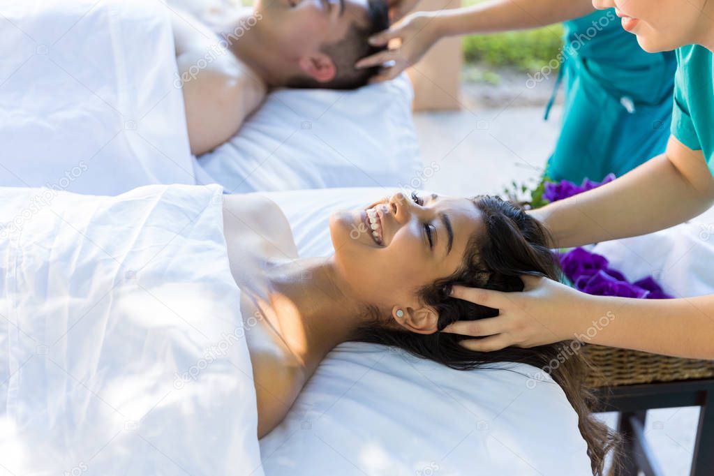Smiling woman enjoying head massage with boyfriend at luxury spa
