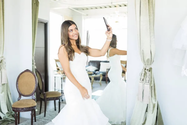 Female shopper trying on wedding dress and photographing herself to post pictures online