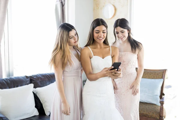 Beautiful bride with her best buddies checking out pictures on mobile phone in living room