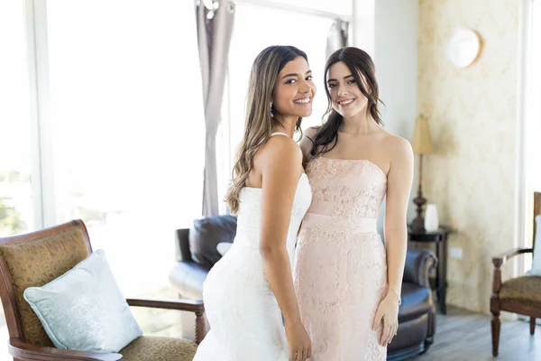 Gorgeous bride and bridesmaid in elegant dresses smiling while looking at camera