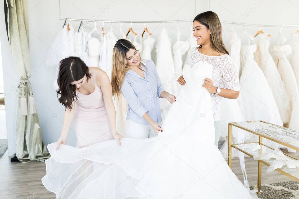 Cheerful young women having fun during bridal gown fitting in wedding fashion store