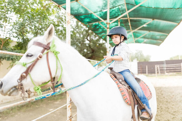 Очаровательный ребенок тянет за собой свинец, сидя на белом коне на ранчо
