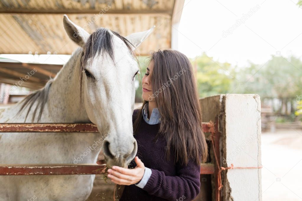 Woman with long brown hair feeding horse while standing at fence at ranch